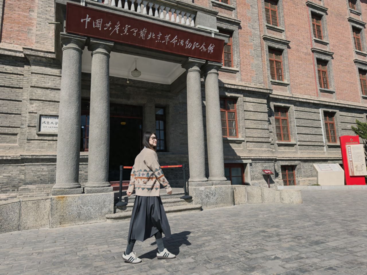 The model stands at the entrance, and the photographer stands face to face, 2 meters apart, with the camera position slightly lower to capture the memorial's logo.

1. Photography poses:
   ①The model stands at the main entrance with hands placed in front or naturally at the sides, legs positioned one in front of the other, and looks up towards the red characters on the entrance;
   ②The model walks from left to right and looks back at the photographer, who takes a low-angle shot and captures the moment.

2. Wardrobe suggestions: Opt for a white fitted cardigan or a solid-colored base shirt on top, paired with loose wide-leg pants or casual suit pants to achieve a relaxed and casual look.