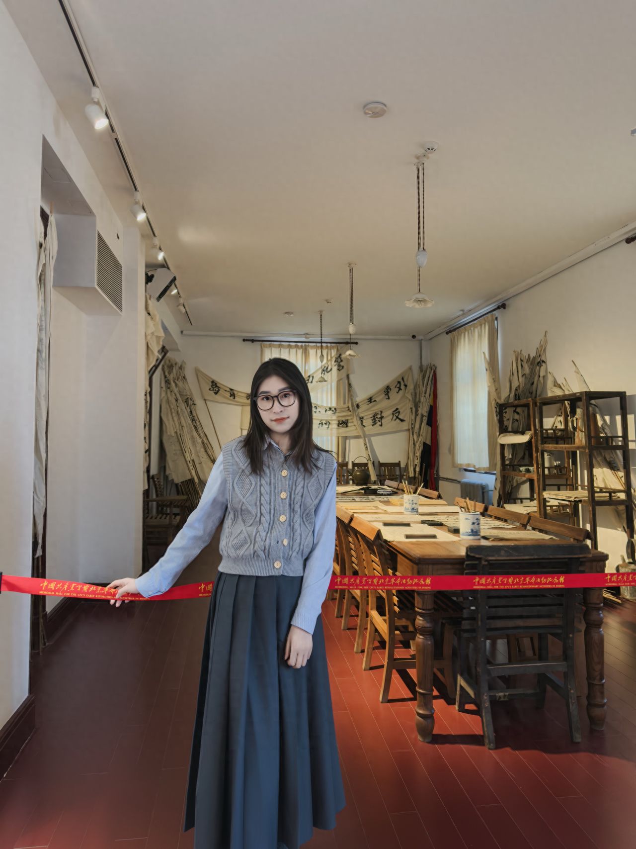 The model stands against the wall, with the photographer positioned face-to-face, 2 meters apart, using a 35mm focal length for a wide-angle shot, trying to capture the background decorations in full.

1. Photo poses:
   ① The model holds a vintage handbag or purse with a slight tilt of the body, and can look at the camera or towards the exhibition hall;
   ② The model stands facing the photographer with hands crossed in front, slightly leaning forward, and can look at the camera or into the distance.

2. Wardrobe suggestions: Opt for a vintage shirt paired with a waistcoat sweater, and match it with a long pleated skirt in gray or black. Shoes can be small leather shoes or white sneakers.