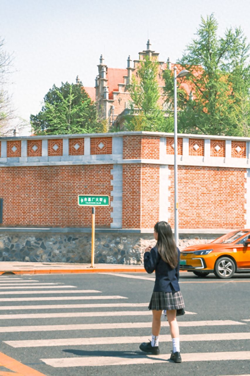 The model stands by the roadside curb, with the photographer facing the model and the building, zooming in the lens from 5 meters away for a low-angle or eye-level shot.

1. Photography equipment: Fujifilm X-H2 with a 16-55mm lens.

2. Poses for the photo:
   ① The model walks on the sidewalk, glancing at the camera or looking to the sides.
   ② The model can also sit on a roadside barrier, sit with arms crossed.

3. Suggested shooting time: It is recommended to go for the shoot between 3-4 PM when the light is soft.