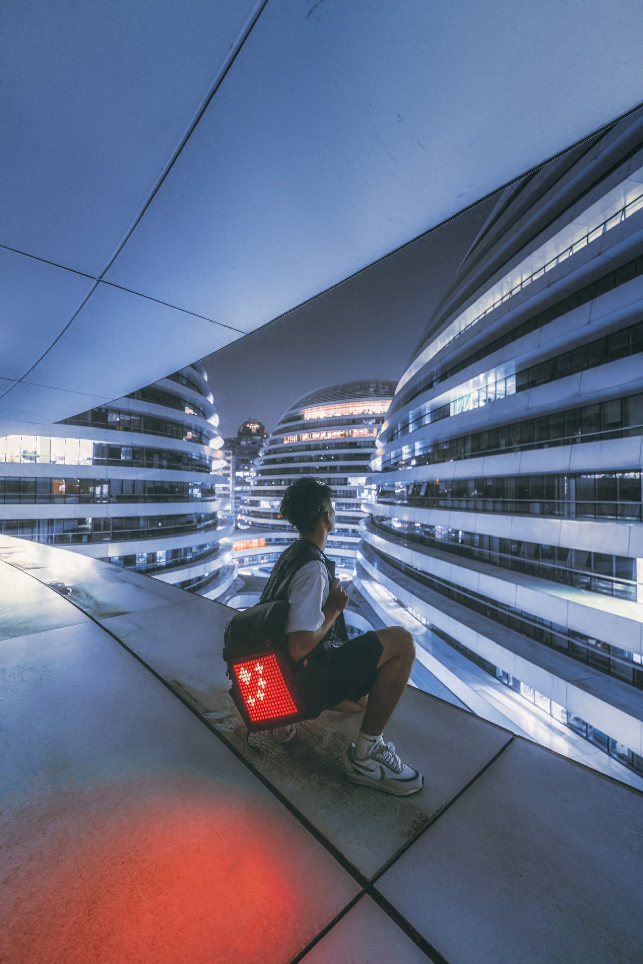 Use a central composition with the subject placed in the middle of the frame to highlight the contrast between the subject and the architecture. The photographer uses a flat angle, including the iconic curvy buildings of Galaxy SOHO in the background and incorporating geometric lines on the ground in the foreground to enhance the sense of space. The model squats with their back to the camera, looking at the building, adding a narrative element to the image. It is recommended to use an ultra-wide-angle lens for shooting. Travel tips: The lighting is on from 18:00 to 22:00 on weekdays, and it may be turned off on weekends, so don't go in vain.