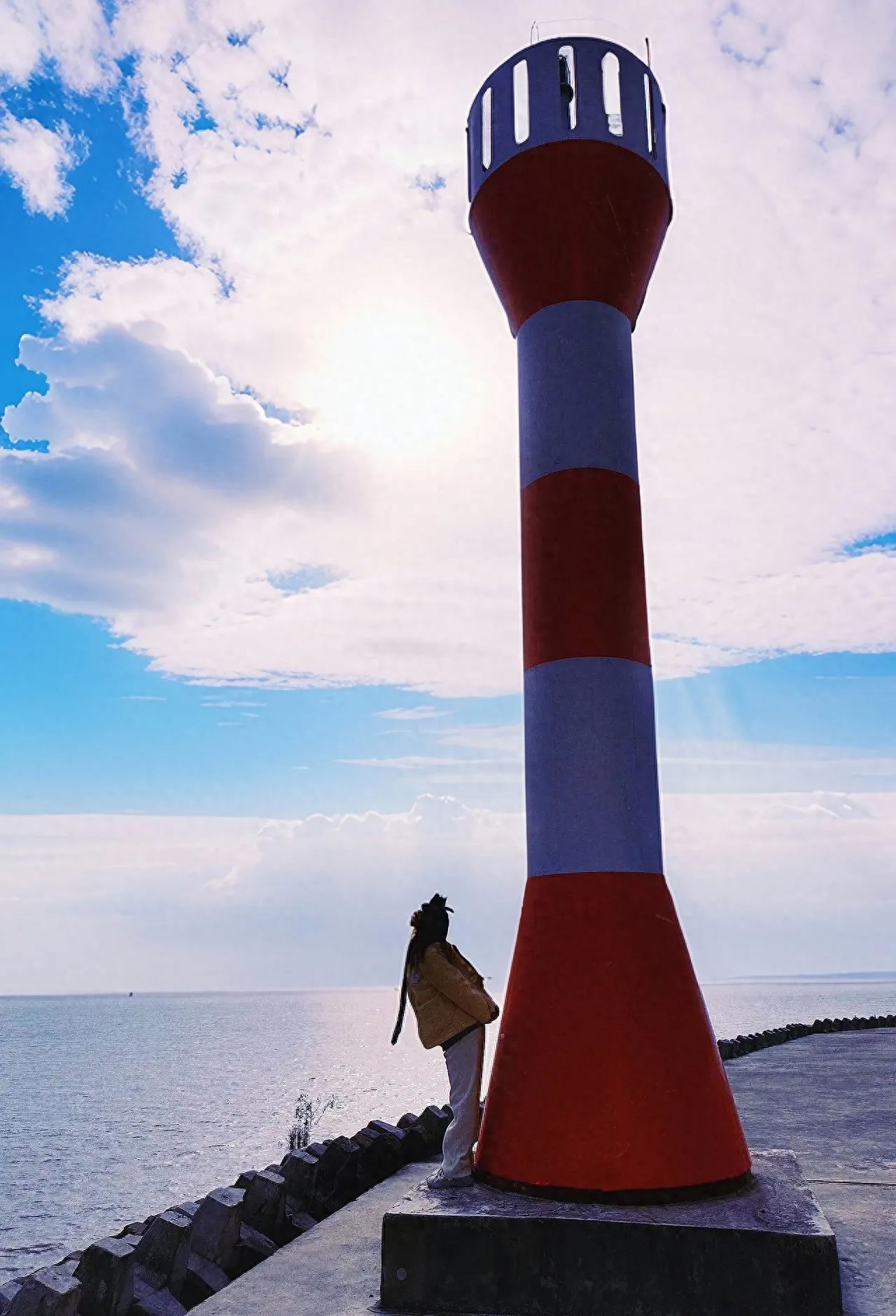 The photographer stands at a side position with a certain distance from the subject and the lighthouse, capturing the scene from a low angle. Using a medium telephoto lens, the color and texture of the lighthouse, as well as the subject's posture, are clearly displayed, creating an open and tranquil atmosphere.

Shooting time: It is recommended to choose a sunny day when the light is good, making it easier to produce good photos.