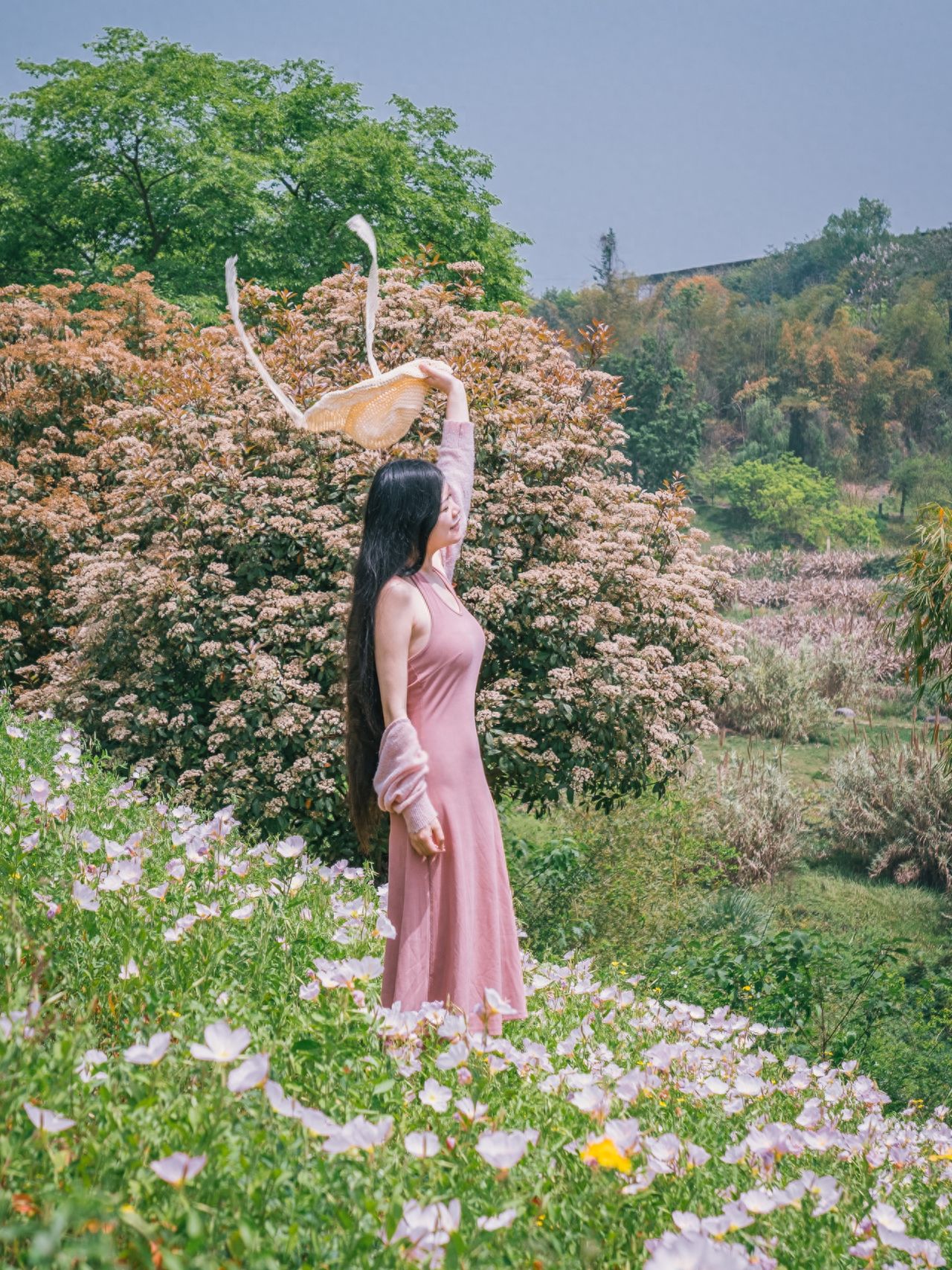 With a backdrop of various trees and evening primrose in the foreground, the person stands amidst the flowers for the photo.