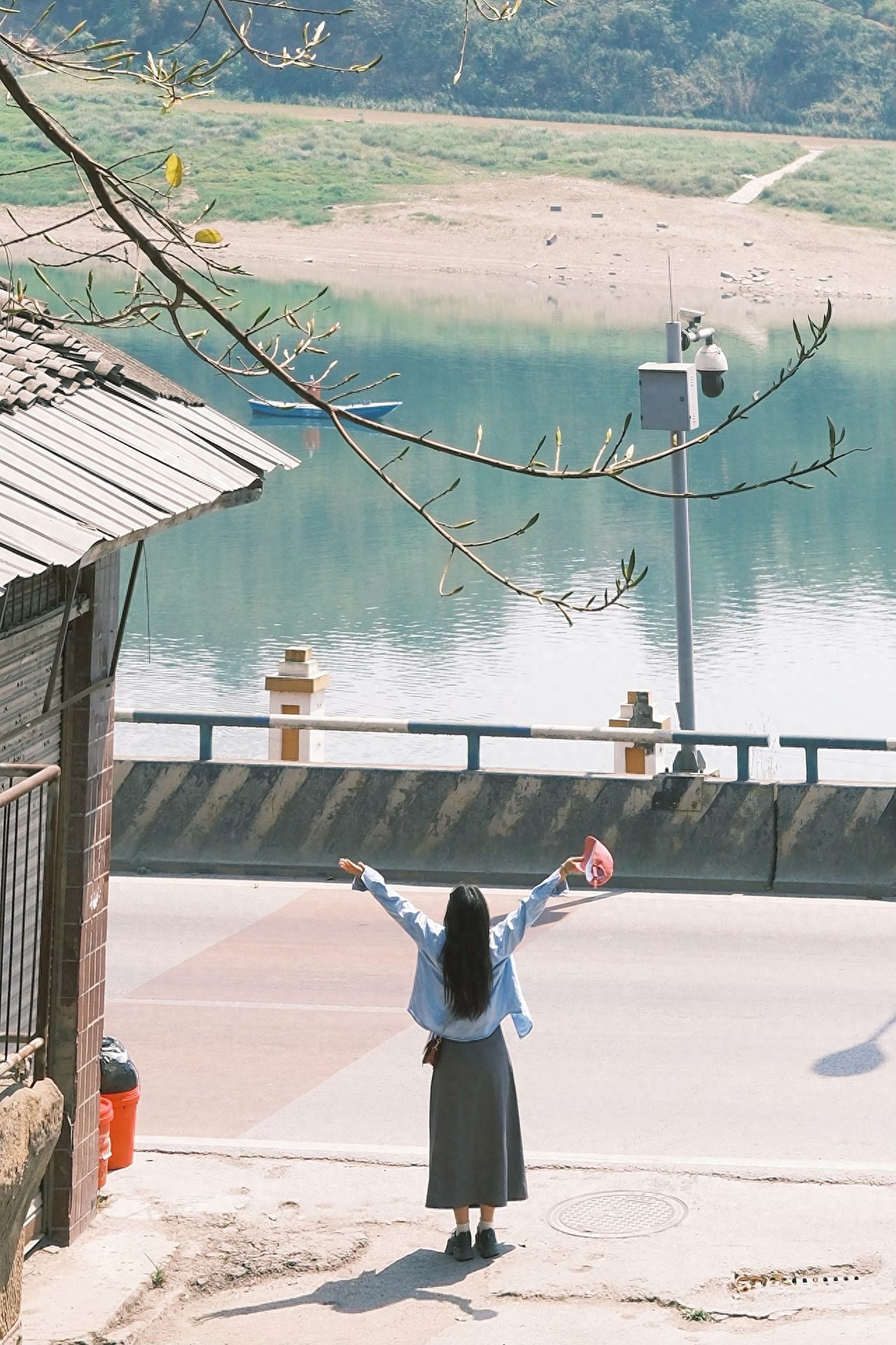Model stands with arms raised and facing the river, stretching upwards and looking into the distance. The photographer is positioned on a step behind the model, shooting from a higher angle with a long telephoto lens or a smartphone zoomed in by 5 times, maintaining a considerable distance between the model and the photographer.

1. Photography Equipment: Fujifilm Xs 20 with a prime 35mm lens.

2. Pose Suggestion: The model should keep their arms open naturally, with one hand holding a hat aloft and the other slightly lowered to add dynamic beauty.

3. Outfit Recommendation: For a riverside shoot, opt for light-colored clothing such as light blue, sky blue, or white to capture a Japanese-style atmosphere that will produce stunning photos.

4. Entrance Fee: Free.