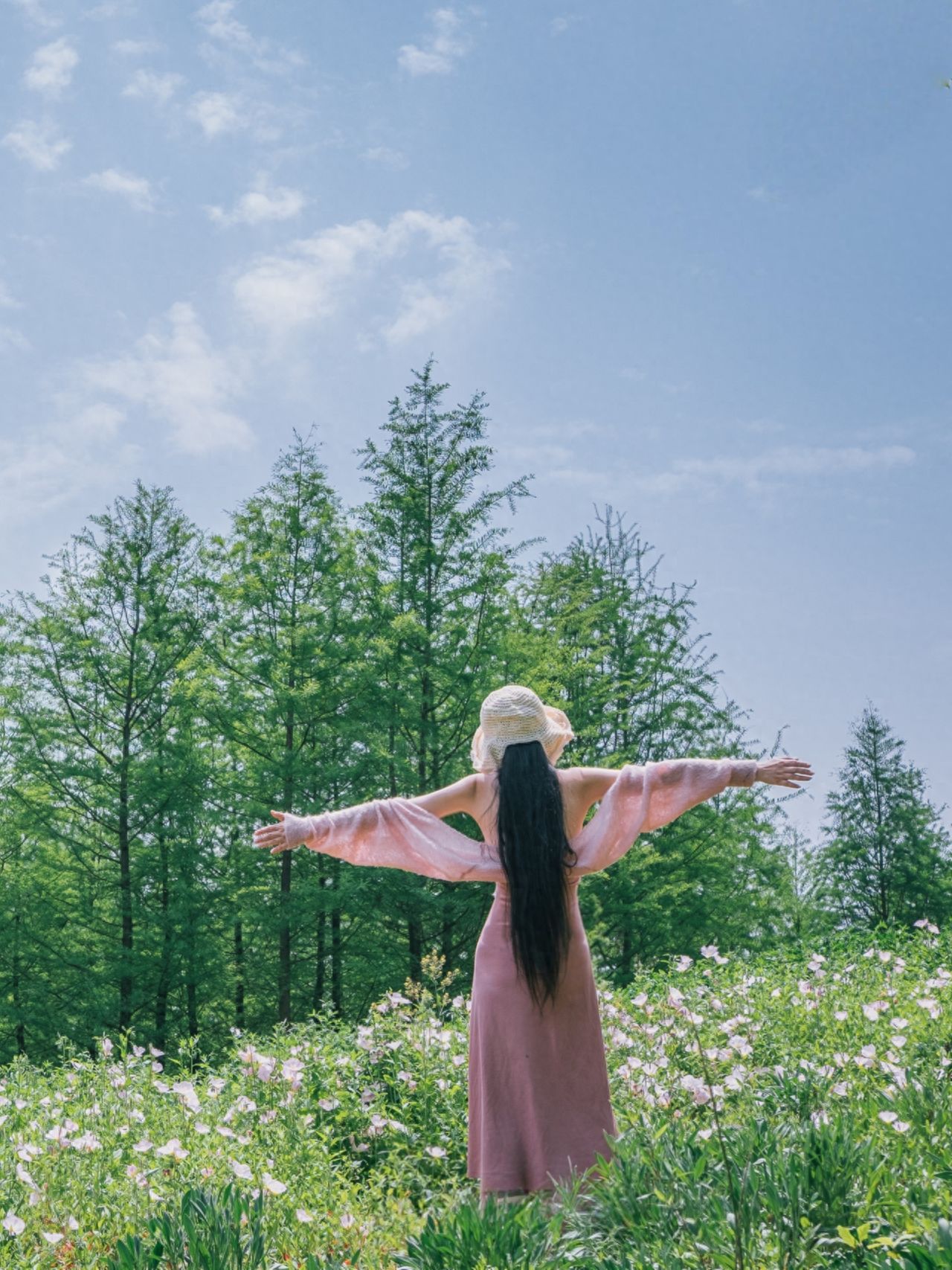 The subject stands amidst the grass, arms wide open facing towards the woods, with the forest and blue sky as the backdrop for the photo. Use blooming flowers by the roadside, rivers, or buildings as backgrounds to enrich the scene. Center composition is used, with the model positioned in the middle of the frame, the blue sky and green woods forming a fresh background, highlighting the integration of the person with nature.

Photography pose: The model naturally extends their arms, enhancing the sense of expansion in the image and the atmosphere of early summer.