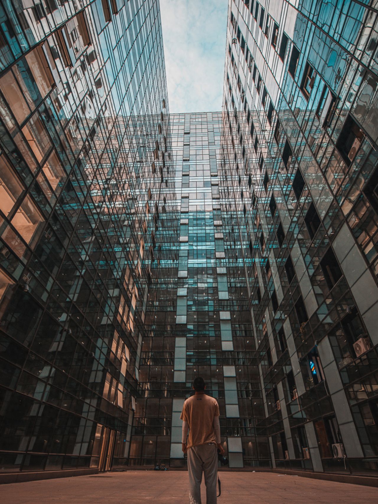 The model stands in the center of the frame, with the photographer positioned directly behind the model, shooting from a low angle to emphasize the depth and grandeur of the architecture. Symmetrical composition is used, with the mirrored glass on both sides of the building forming symmetrical lines, guiding the visual focus towards the center, creating a stable and impactful image.

Pose: The model stands with their back to the camera, hands naturally hanging down, enhancing the narrative and sense of solitude in the image.
