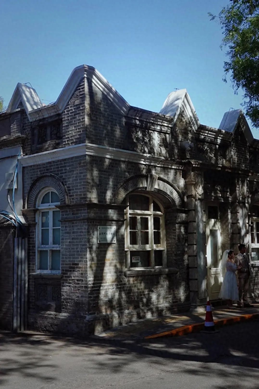 The photographer stands diagonally from the building at a slight distance, using a flat shooting angle with the camera position slightly lower than the building's ridgeline to highlight the architectural sense of three-dimensionality and light and shadow effects. A character is placed on the right side to enhance the storytelling and sense of space.
