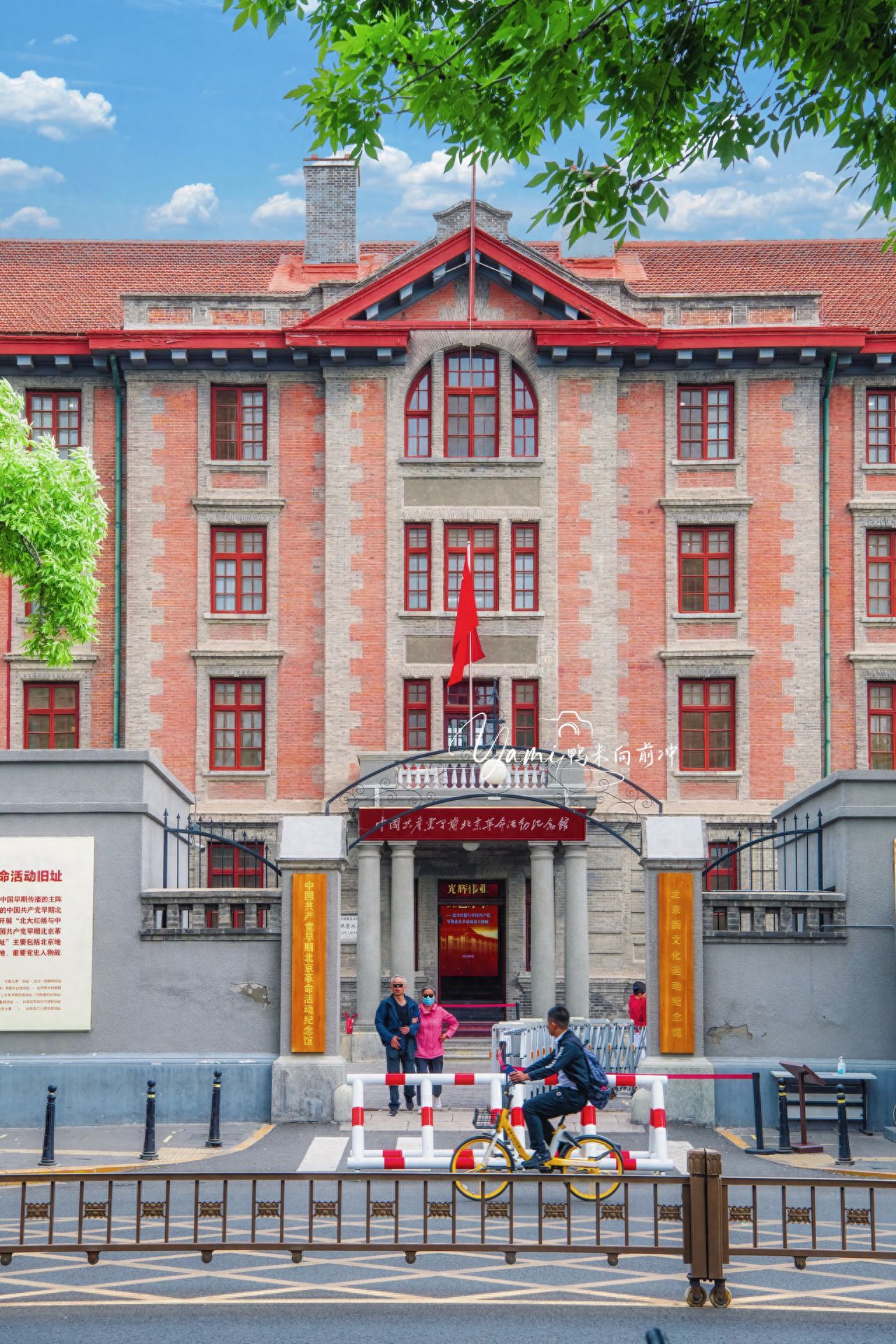 The photographer stands on the sidewalk directly across from the Red Building of Peking University, adopting a flat shooting perspective, directly facing the building to capture the image, ensuring the picture is level and symmetrical. Use central composition to place the main entrance and red flag of the Red Building in the center of the frame, highlighting the symmetry and solemnity of the main building. When framing, center on the main body of the Red Building, appropriately retain the red tiles at the top and the street below, and introduce a small amount of green leaves at the top of the image as the foreground to increase the sense of depth and vitality in the picture.

Travel Tips:
① It is recommended that you make an appointment in advance through the public account, and admission is free; ② Opening hours are from 9:00 to 17:30 every day, closed on Mondays.