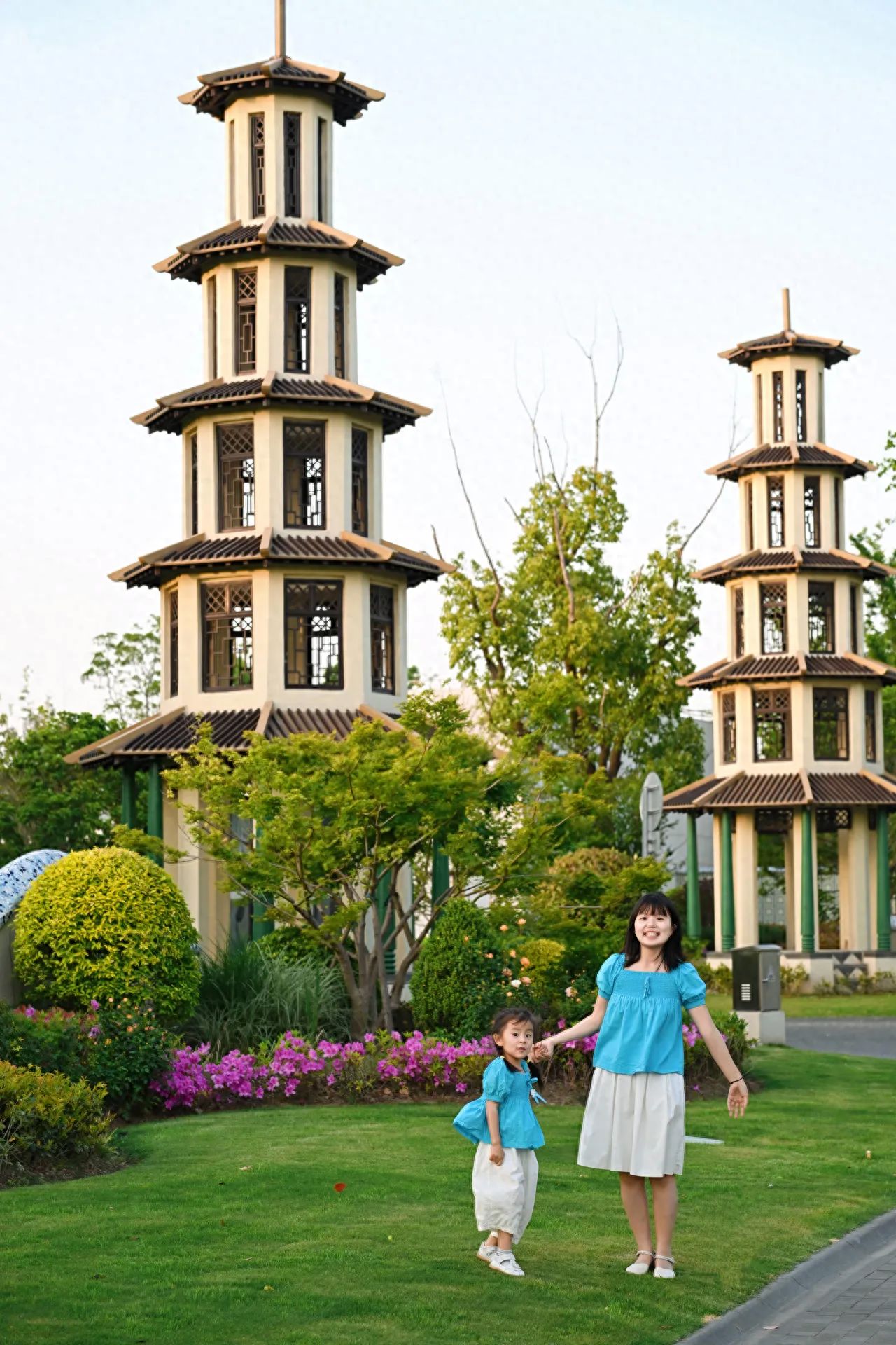 The model stands on the lawn, with the photographer in front of the model, shooting from a low angle to capture the tower in its entirety. Use a standard lens for the shot, with the model positioned at the bottom right of the frame, and the background featuring the tower and sky.

Outfit suggestion: Vacation-style clothing.