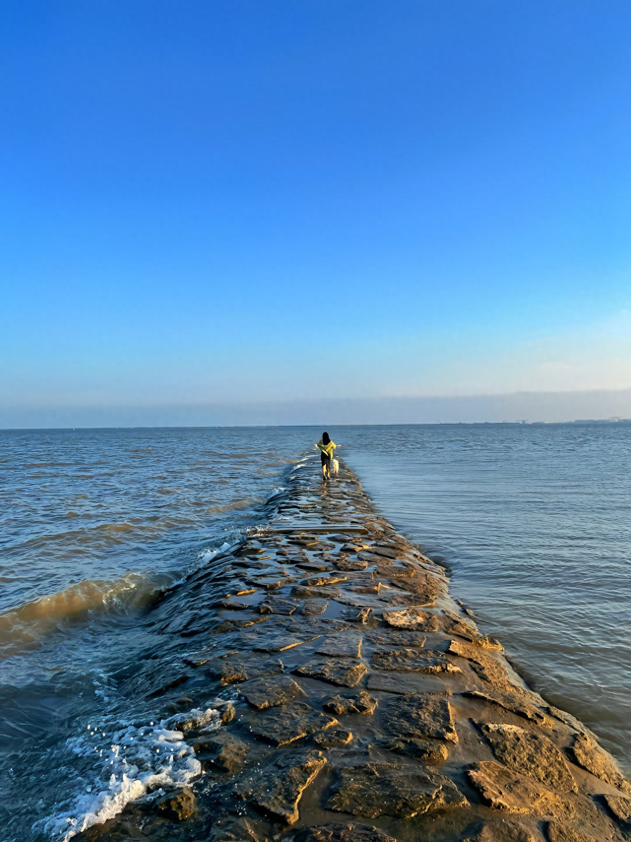 Use leading lines composition to extend the stone path from the foreground to the horizon, guiding the viewer's attention to the model. Place the model in front of the stone path and the photographer behind it for a low-angle shot, capturing the person at the junction of sea and sky. Include the stone path, ocean, and blue sky in the frame to enhance the sense of depth.

Additional tips: Choose a clear day for shooting to achieve a more open and transparent image.