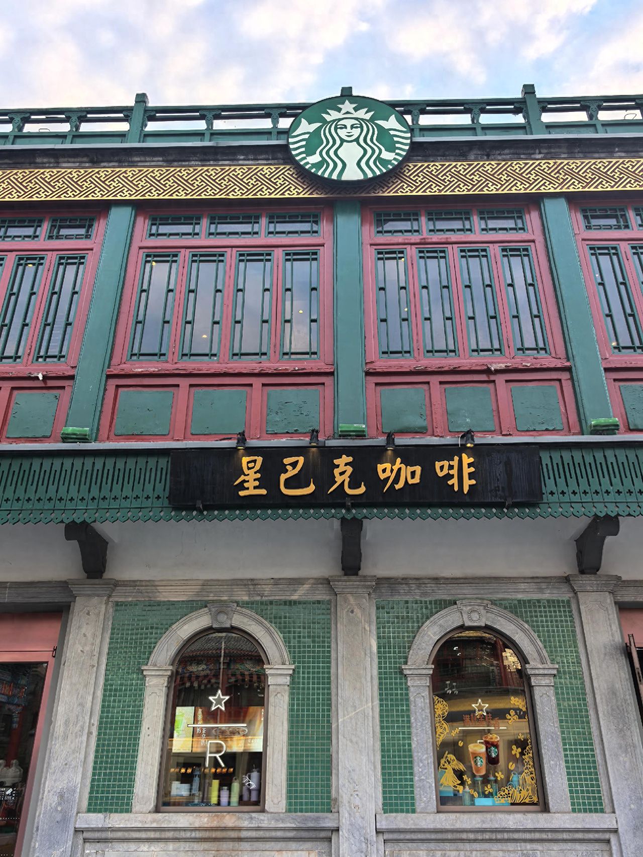 Place the Starbucks logo, Starbucks Coffee sign, and the main building in the frame, with a symmetrical balance between the left and right. Include both the building and the sky above in the shot, highlighting the traditional architectural features.