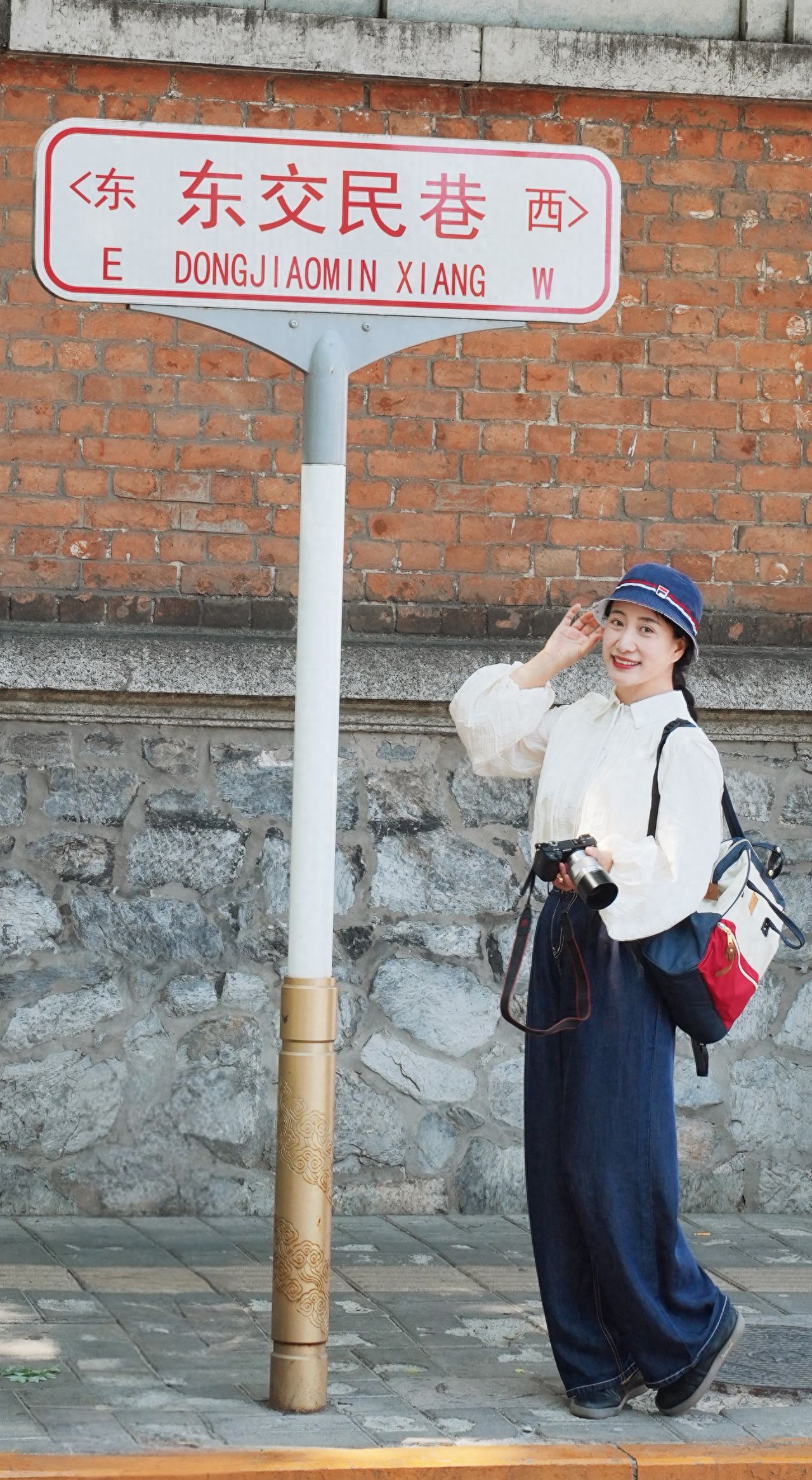 The model stands to the right of the road sign, positioned on the right side of the frame, with the photographer using a low-angle shot to highlight the road sign and red brick wall. The subject is placed on the right, the road sign is in the central upper part of the image, and the red brick wall serves as a backdrop to enhance the scene. 

Travel Tips: Admission is free.