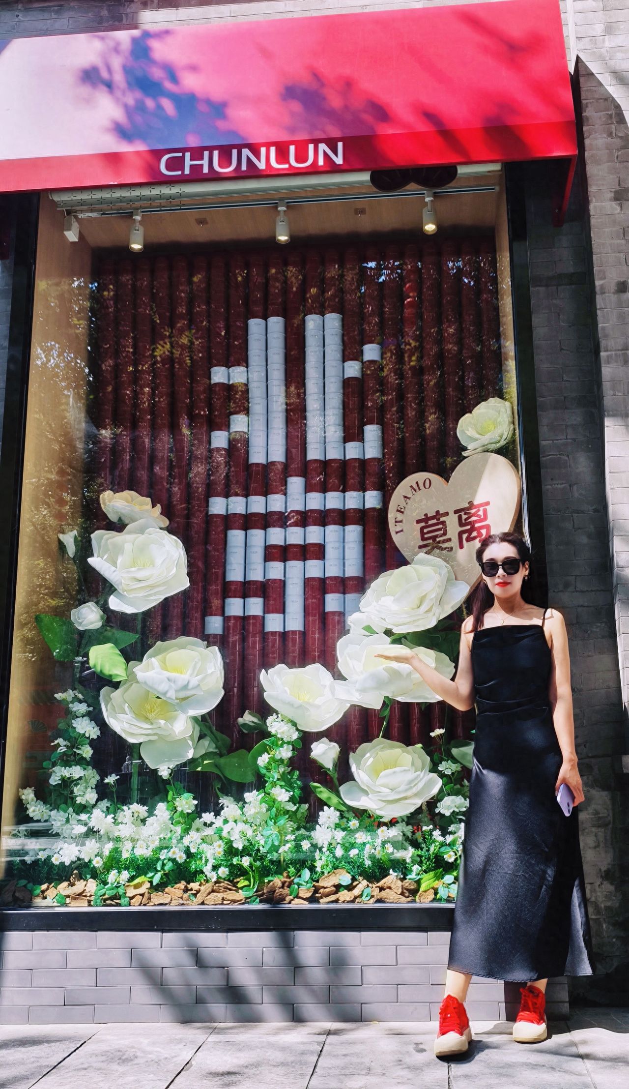 The model stands to the right of the window, positioned at one-third of the image from the right. The photographer uses a low-angle shot. The composition follows the rule of thirds, including the "Moli" heart-shaped decoration inside the window, white roses, and the red "CHUNLUN" sign above. The model lightly touches the roses with her side body, interacting naturally. It is recommended to use a standard focal length lens to capture, preserving the background details.

Travel Tips: Free check-in available in front of the door.