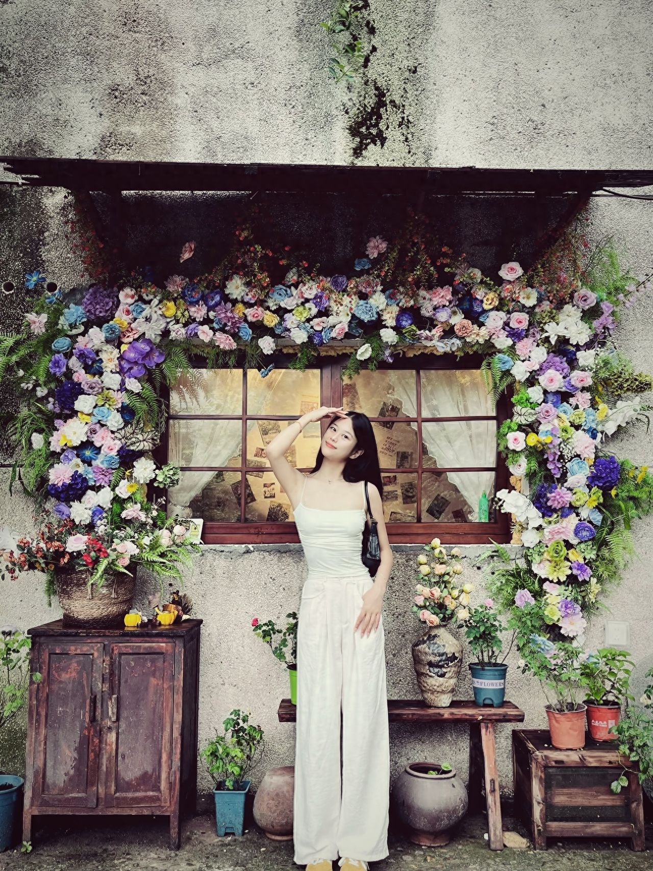 The subject is positioned in the center of the frame, highlighting the main focus. The photographer uses a frontal angle to capture the full view of the floral green wall as the foreground frame, with the background including windows and mottled walls to add depth. The model supports her forehead with one hand, tilts her head, and smiles, making a natural and vivid gesture that enhances the interaction in the image.

Travel Tips: The entrance fee is free.