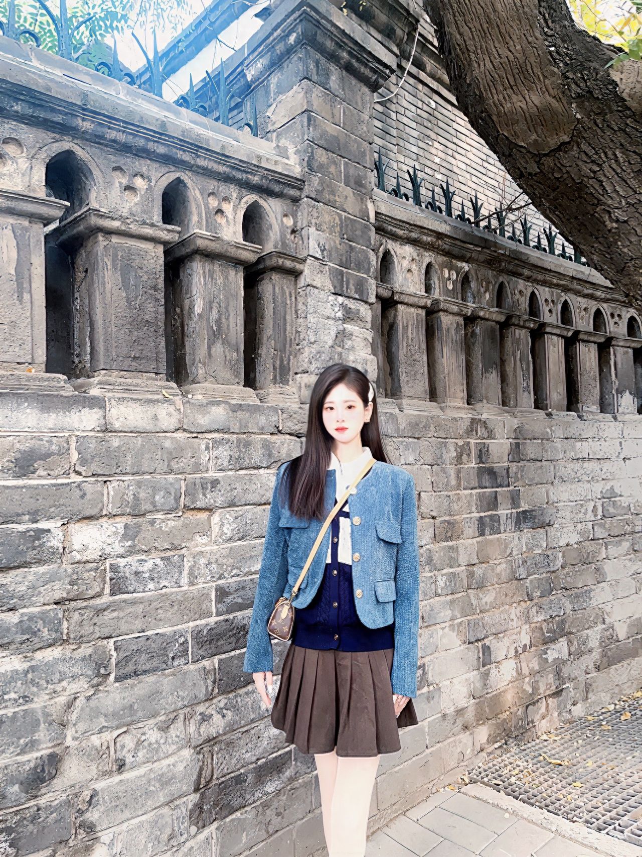 Model stands against a grey brick wall, shot from a flat angle, positioned slightly below the center of the frame, using the rule of thirds composition. The vertical lines of the arched stone columns in the background serve as leading lines, enhancing the sense of depth. The view includes the texture of the brick wall and architectural details above, highlighting a sense of history.

Outfit suggestion: It is recommended to wear modern Chinese, vintage Western attire, or preppy styles.