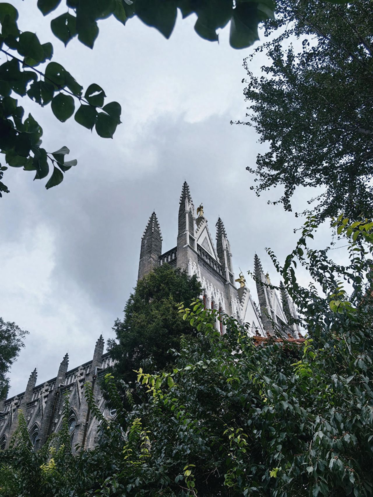Photo by Xishiku Catholic Church - Capturing the gray spire through the foliage.