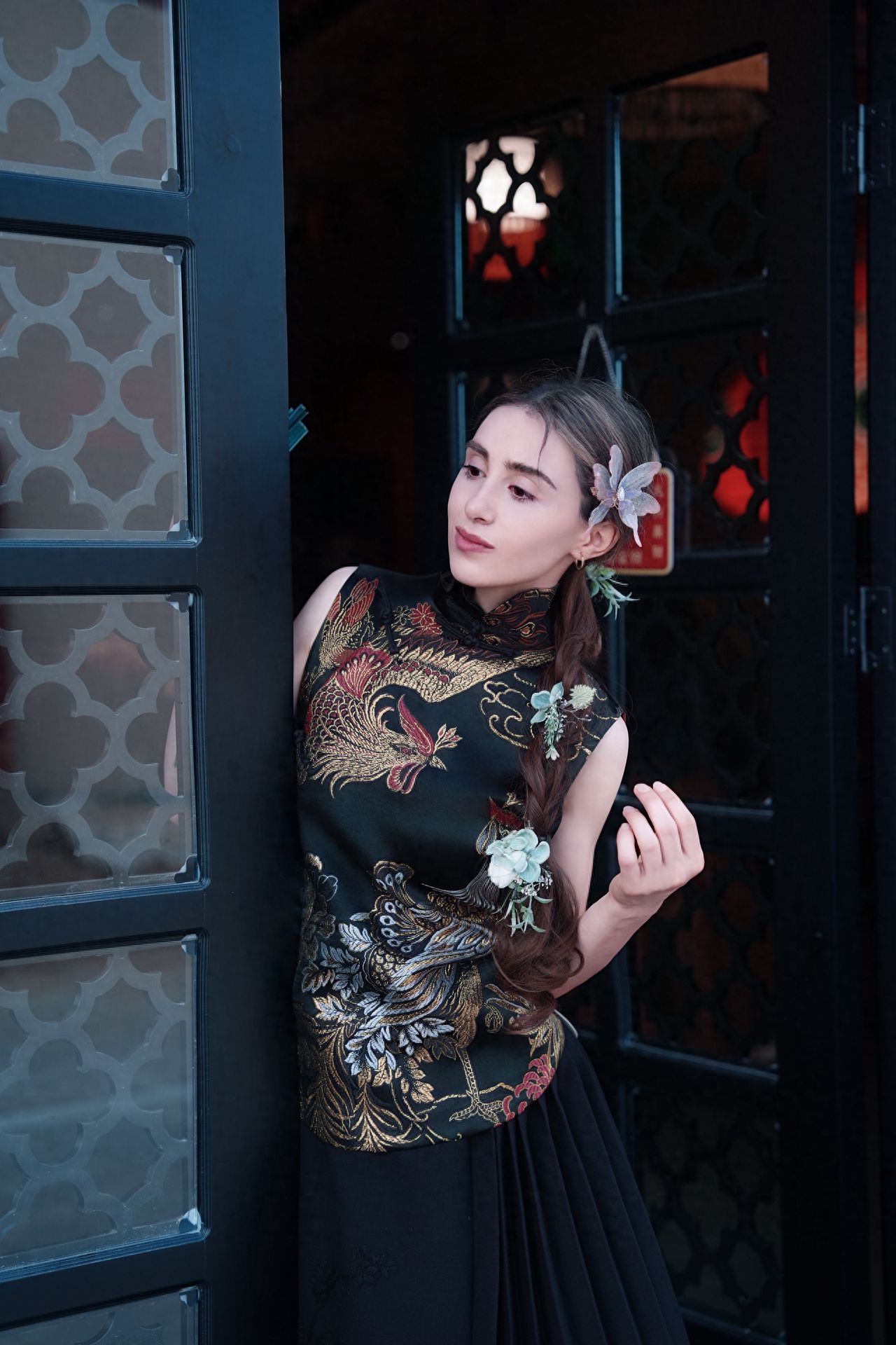 Utilize the frame composition by employing the patterned door frames on both sides to naturally highlight the model. Position the model within the door frames, centrally located in the frame. Have the model lean against the door frame with a side pose and raise their hand in a natural gesture to add liveliness. Include the door frame patterns and the dark background within the shot to enhance the sense of depth.