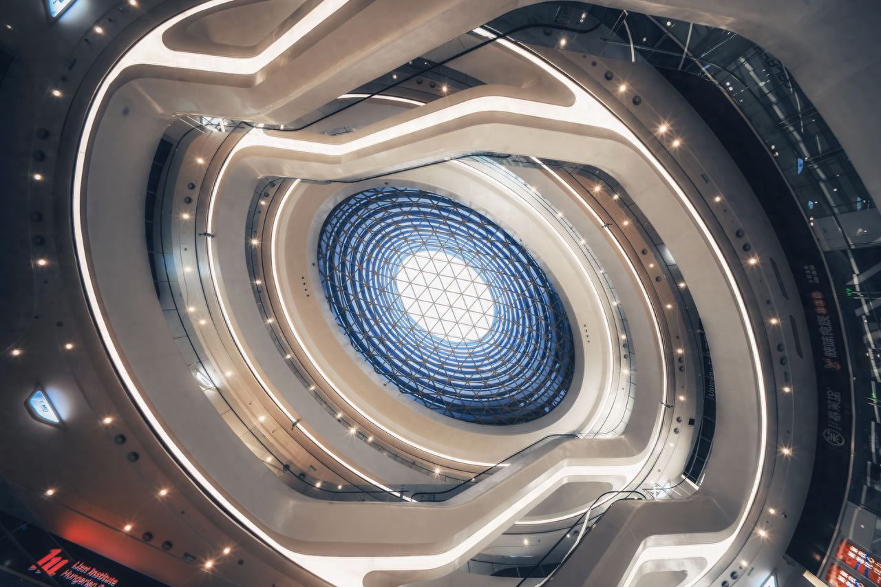 The photographer stands directly under the dome, using a low-angle shot to place the glass dome at the center of the frame. The composition is symmetrical, with the circular architectural lines extending outward from the center as leading lines to enhance the sense of depth. The shot should include the entire dome and multiple circular structures, highlighting the symmetrical beauty and spatial hierarchy of the building.

Equipment settings: Sony A7M4, Viltrox AF 14mm F4.0.