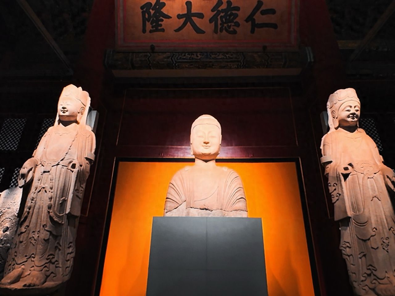 The photographer stands directly in front of the Buddha statue, using a low-angle shot, with the plaque and the Buddha as the central axis for symmetrical composition. The stone statues on both sides are evenly distributed across the image, highlighting the Buddha and the plaque in the center. The frame includes the Buddha statue, the stone statues on both sides, and the Ren De Da Long plaque above. The red interior walls and top decorations of the building are retained. A wide-angle lens is used to ensure symmetrical balance in the image, showing an overall sense of solemnity.

Travel Tips: Purchase tickets on the Forbidden City Museum's WeChat mini-program one week in advance. Avoid going empty-handed and enter the palace as early as possible in the morning. Start with the central axis tour to avoid peak crowds.