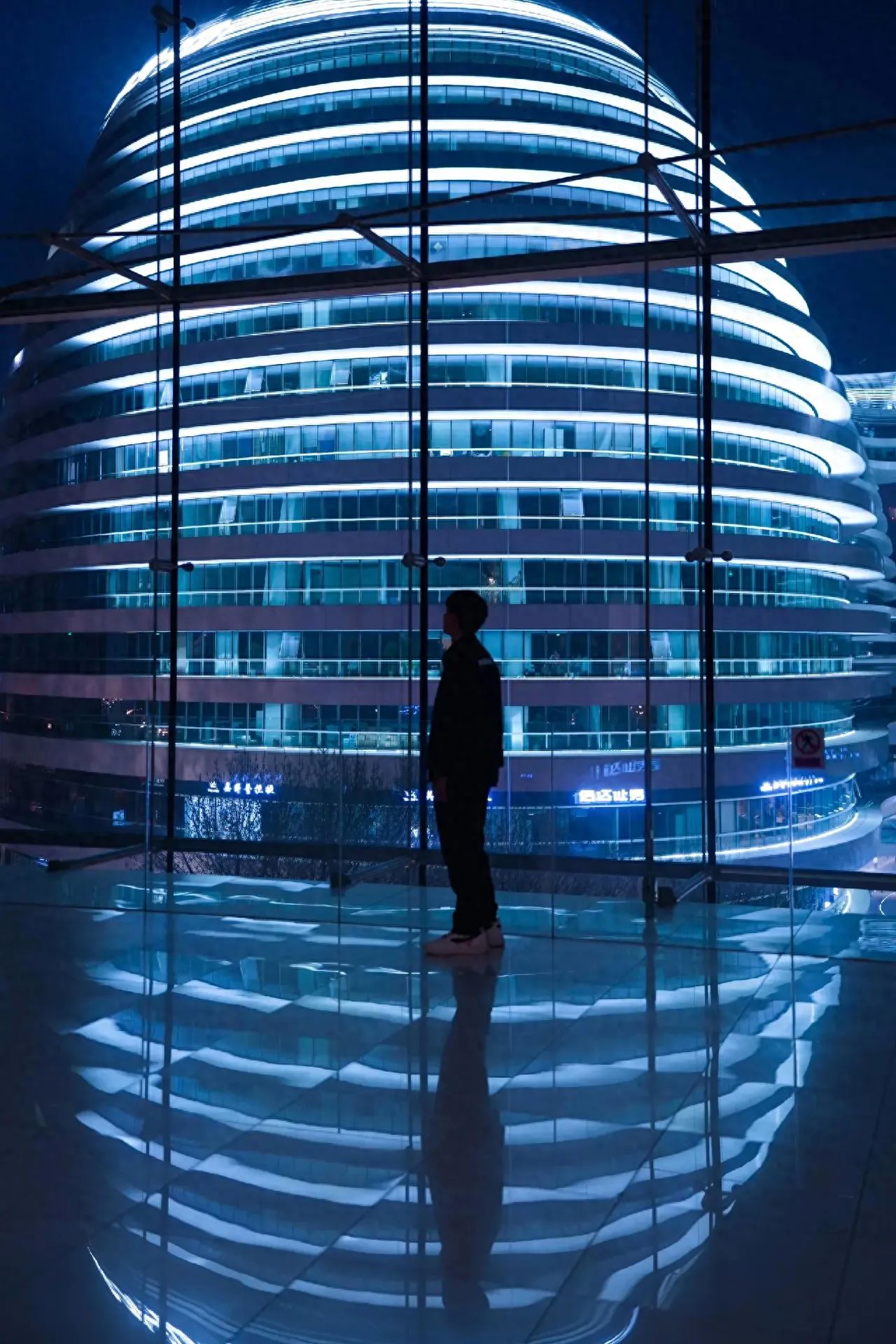 1. Camera Position: The photographer stands behind and to the side of the subject, shooting from a flat angle.
2. Composition Techniques: Contrast composition is used, with the subject's black attire contrasting against the illuminated building to create a light and shadow contrast; Symmetrical composition is employed, with the subject's reflection on the smooth ground forming a symmetry with the person, enhancing the aesthetic appeal of the image; Frame composition is utilized, with the border of the floor-to-ceiling window acting as a frame to enclose the building and the subject, highlighting the main focus.
3. Lens Usage: A wide-angle lens is used to capture a large area of the building and the reflective effect of the ground, enhancing the sense of space and visual impact.
Shooting Time: On weekdays in the evening, there are really few people, highly recommended for friends to go in the afternoon when there are almost no crowds.