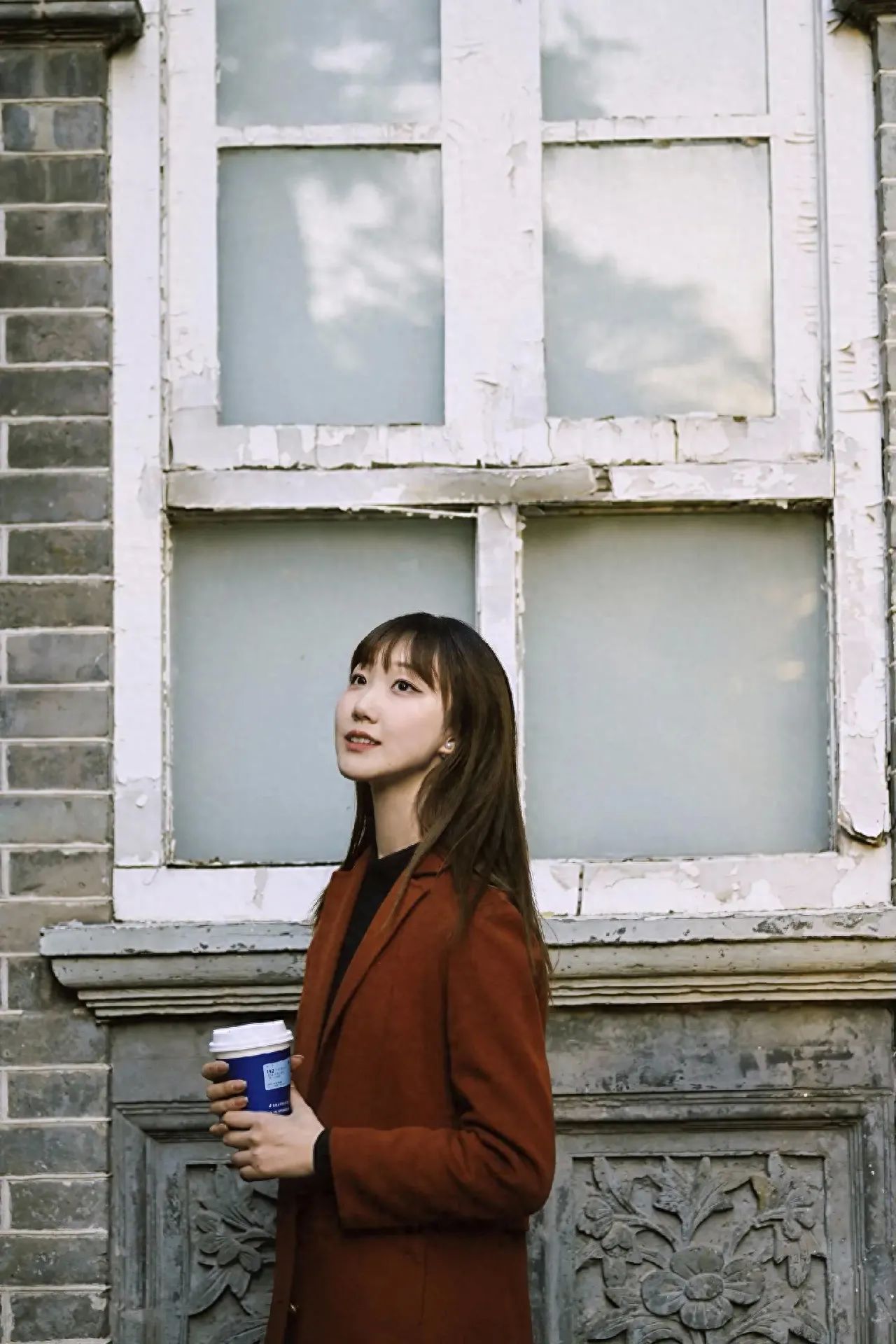 The model stands by the window, and the photographer slightly below the model's eye level shoots upwards at a slight upward angle, enhancing the sense of depth and the feeling of looking up in the frame. A centered composition is used, with the window frame forming a natural background frame. It is recommended to use a medium focal length lens for shooting.

1. Equipment settings: Nikon Z30, Nikkor Z 50mm f/1.8 S.
2. Pose suggestion: The model can stand sideways, slightly tilt the head back, and hold a coffee cup.
3. Travel tips: It is recommended to choose autumn for shooting, as Beijing's autumn has a unique photographic style, suitable for producing quality photos.
4. Props: A coffee cup can be used as a prop, held by the model.
5. Additional advice: Please pay attention to weather changes and dress warmly in a timely manner.