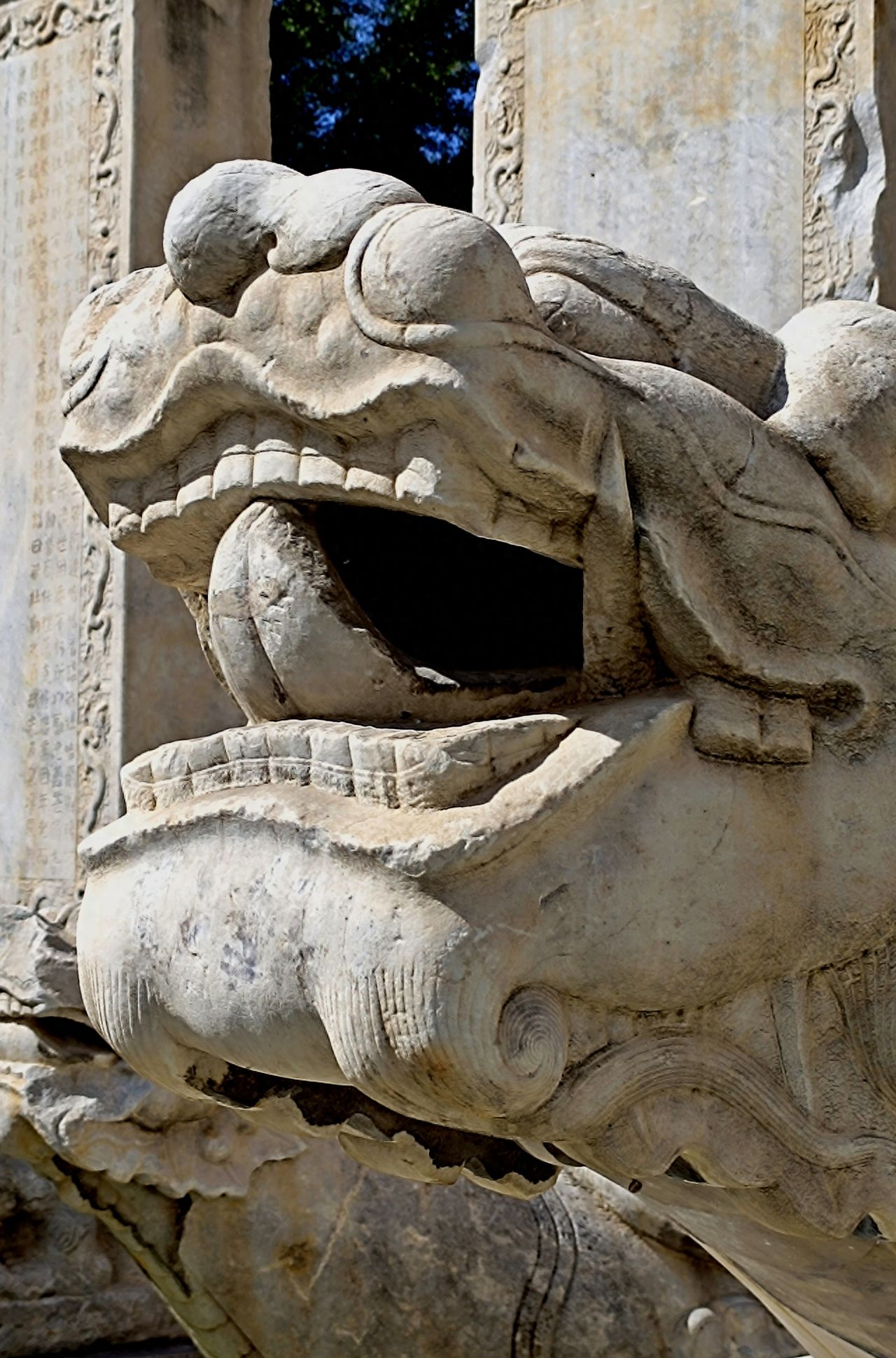 Photo by Beijing Stone Carving Art Museum - Close-up of the stone beast head with tongue sticking out under a stone stele.