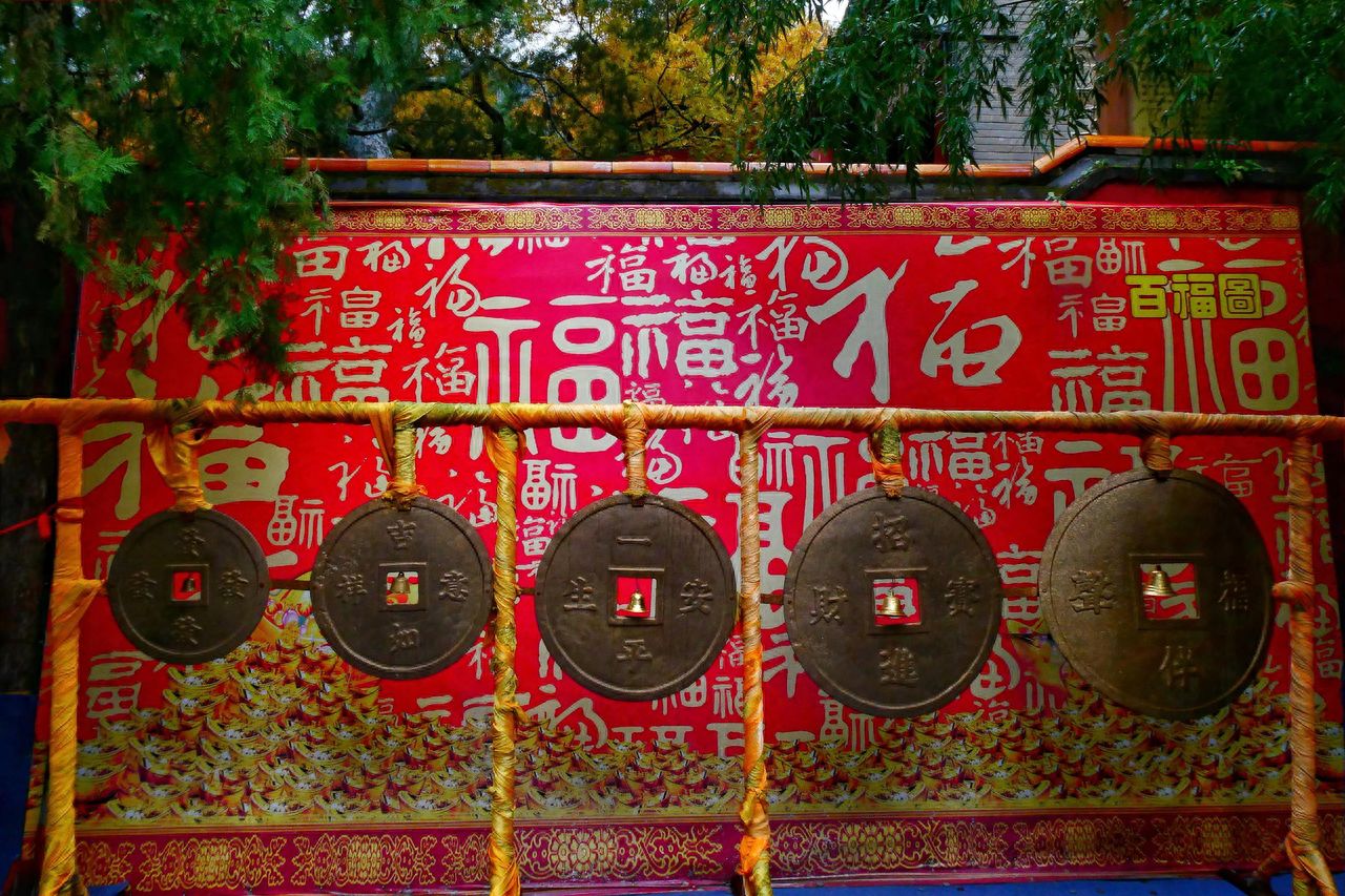 Photo by Tan Zhi Temple - Copper Money Installation in Front of the Red Wall with the Character 'Fu'